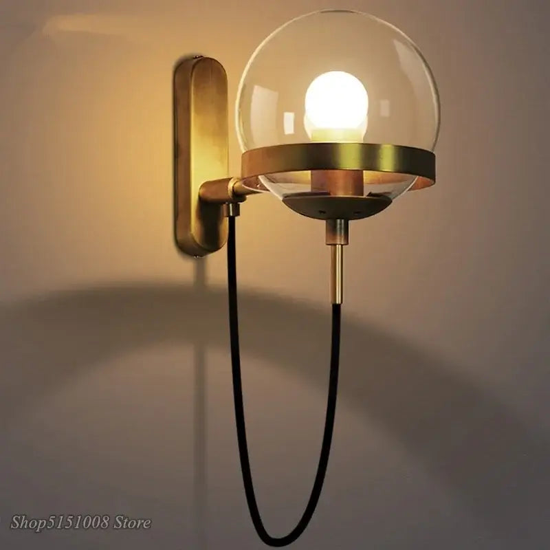 Modern brass and glass globe led wall lamps featuring a brass finish, clear glass globe, and black fabric cord for bedroom use