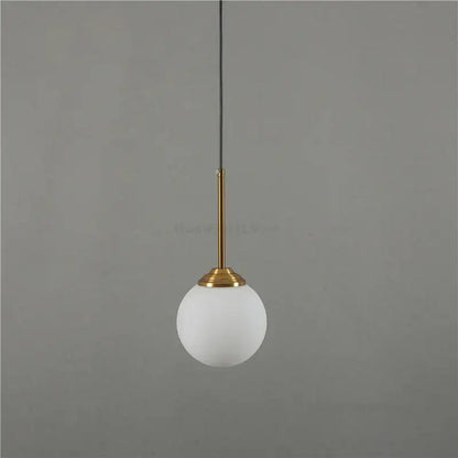 Modern brass and glass pendant lights featuring a frosted white glass globe suspended by a slender brass stem for kitchen dining room
