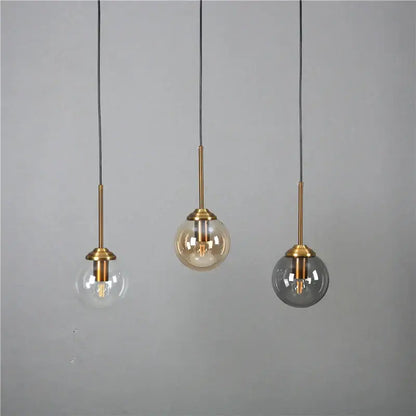 Three modern pendant lights with brass stems and clear amber and smoked gray glass pendant shades for kitchen dining room