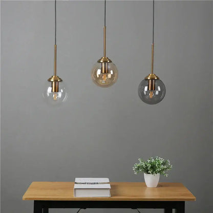 Modern brass and glass pendant lights with clear amber and dark gray glass pendant shades hanging above a wooden table