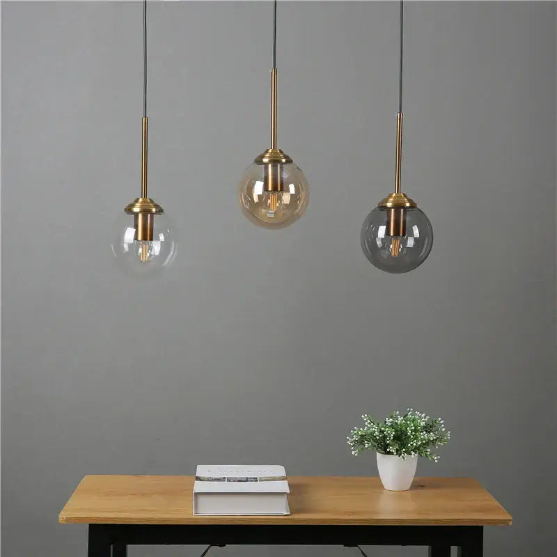 Modern brass and glass pendant lights with clear amber and dark gray glass pendant shades hanging above a wooden table