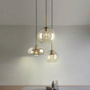 Three modern pendant lights with clear glass globes and brass accents hang from black cords for kitchen or dining room