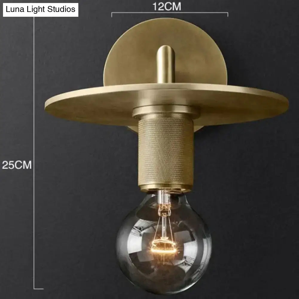 Modern brass and glass wall sconce with circular backplate textured cylindrical stem and exposed bulb for bedroom lighting