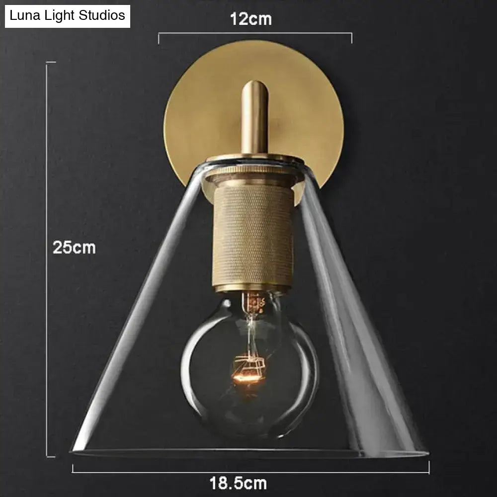 Modern brass and glass wall sconce with clear glass conical shade and exposed filament bulb for bedroom lighting