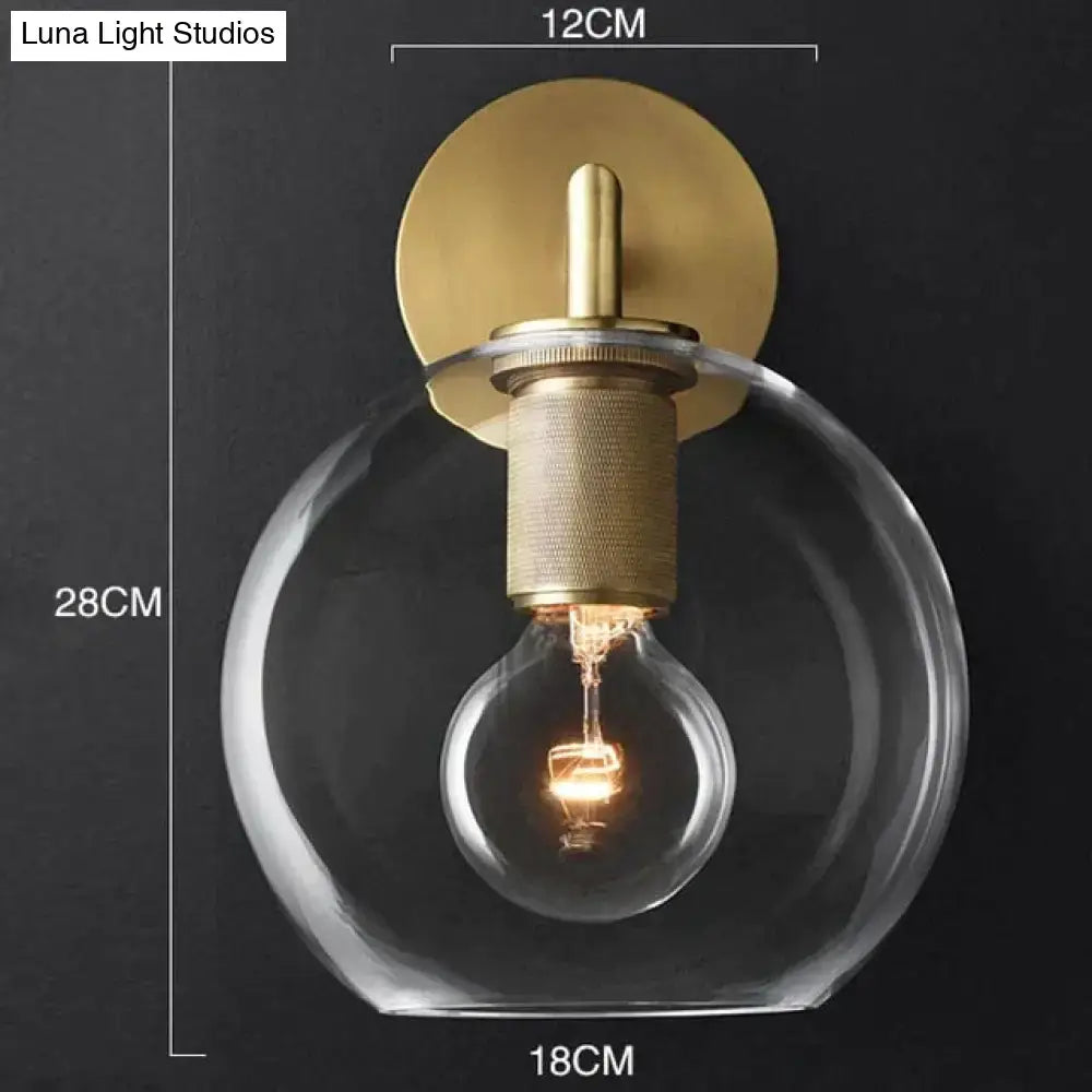 Modern brass and glass wall sconce with clear glass globe and exposed filament bulb for bedroom lighting