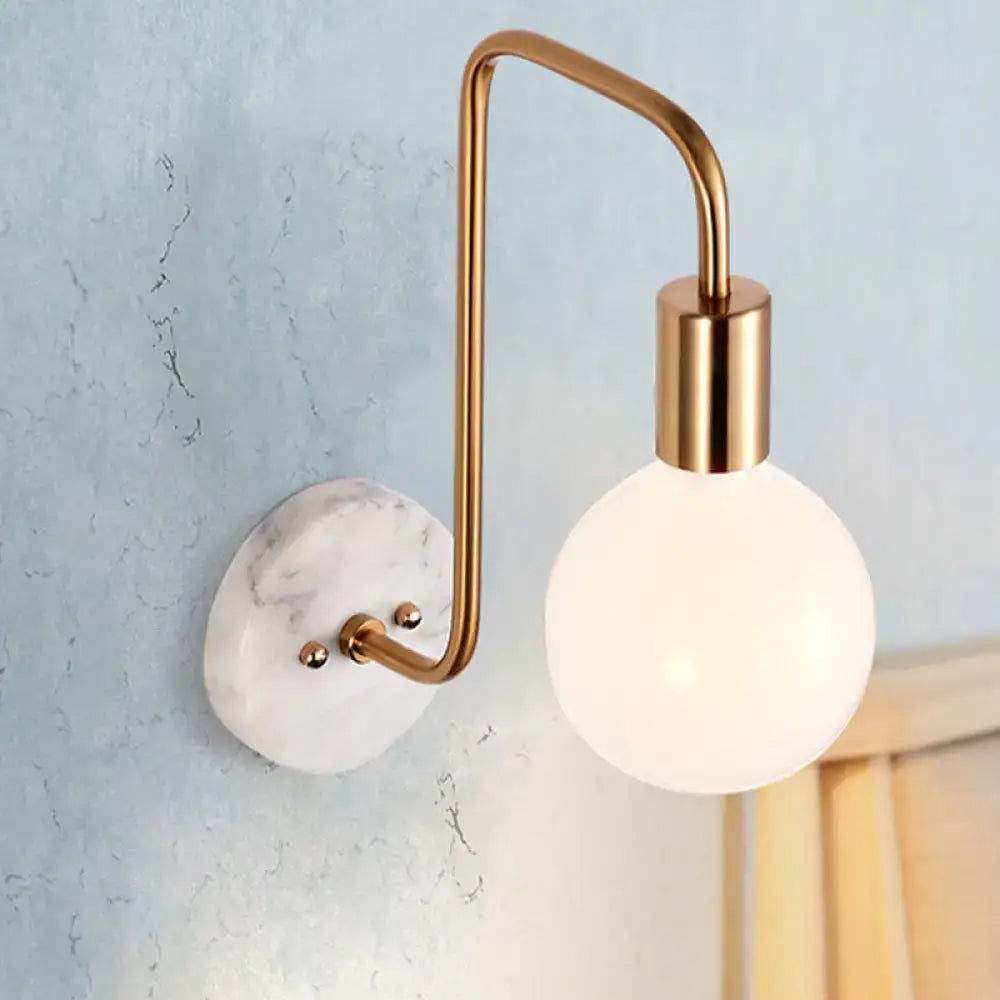 Modern brass and marble wall lamp with a white glass sconce and curved arm mounted on a white marble backplate