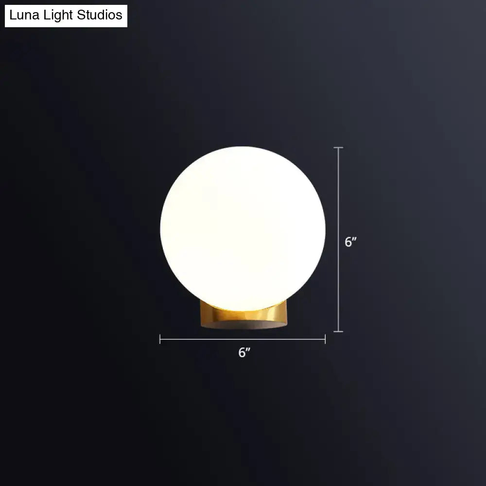 A sleek 6-inch round wall mount lamp with frosted white opal glass shade and polished brass base for bedroom use