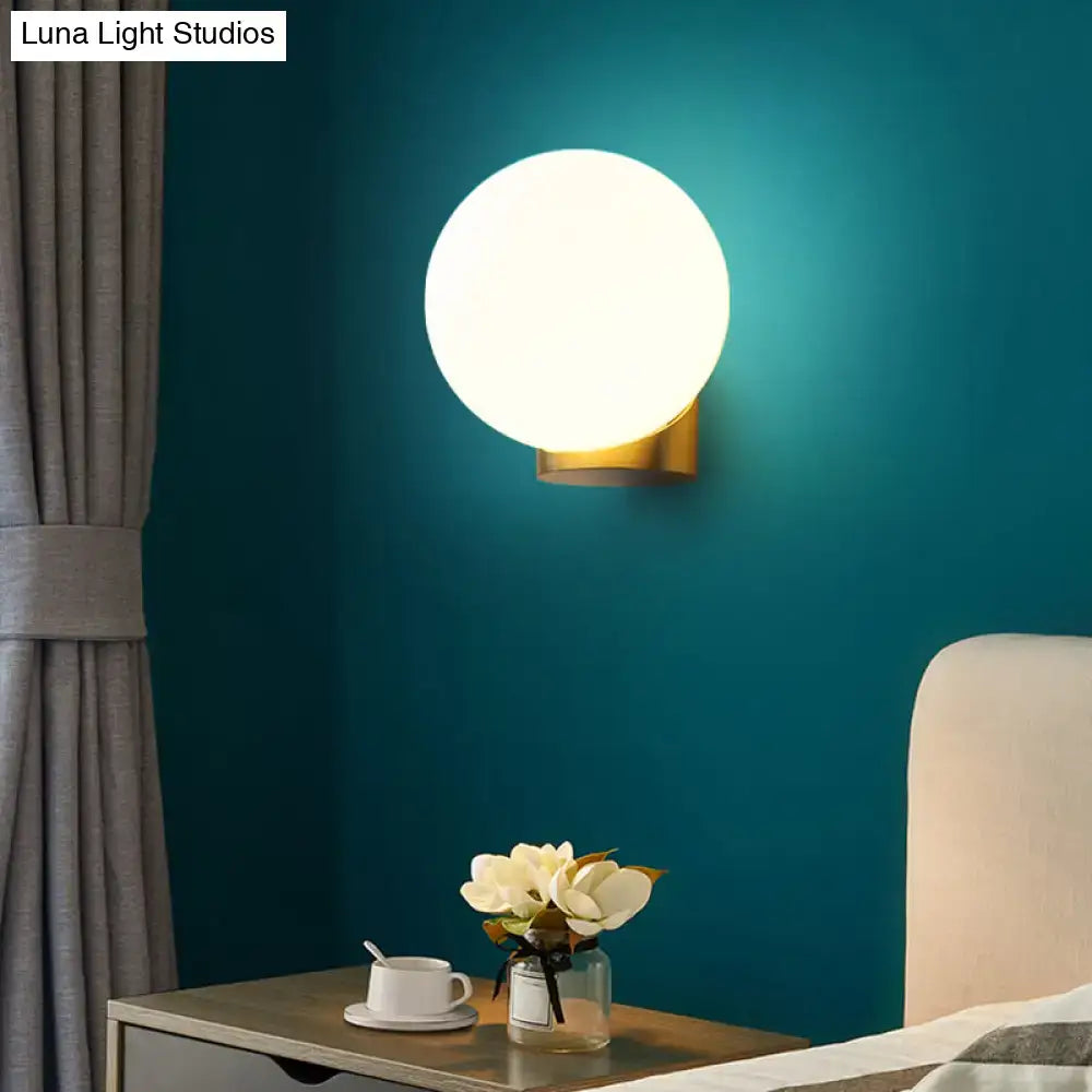 Modern brass and opal glass wall mount lamp with round glowing white globe and sleek gold-finished base for bedside