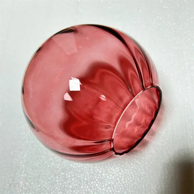 Modern brass and pink glass wall lamp featuring a translucent ruby red globe with subtle internal swirls for living room decor