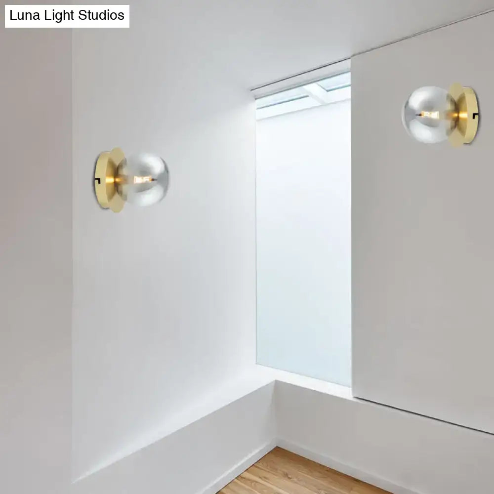 Modern brass wall lamp with gold-toned spherical light fixture and clear glass shade for bedroom lighting