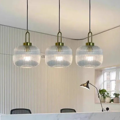 Three elegant glass pendant lights with vertical striped glass and brass fixtures hang for dining room lighting
