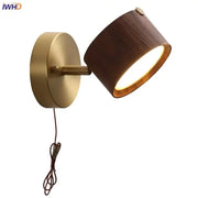 A warm-toned modern brass and walnut led wall sconce with a cylindrical wooden shade for bedroom spotlighting