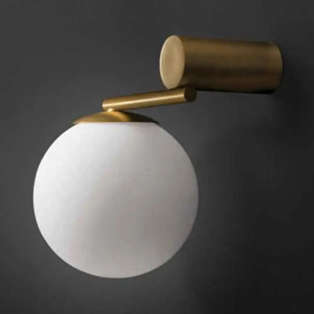 A sleek modern brass wall sconce with a frosted white glass sphere for bedroom lighting