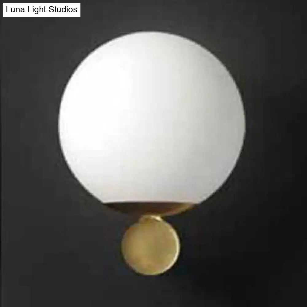 Modern brass and white glass sphere wall sconce featuring a sleek white glass sphere with polished brass base for bedroom lighting