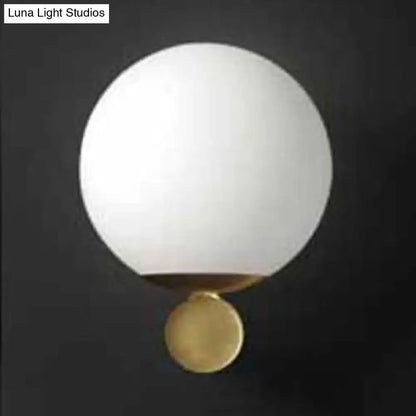 Modern brass and white glass sphere wall sconce featuring a sleek white glass sphere with polished brass base for bedroom lighting