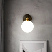 Modern brass and white glass wall sconce with gold-toned sphere, frosted white glass globe, and matte black backplate
