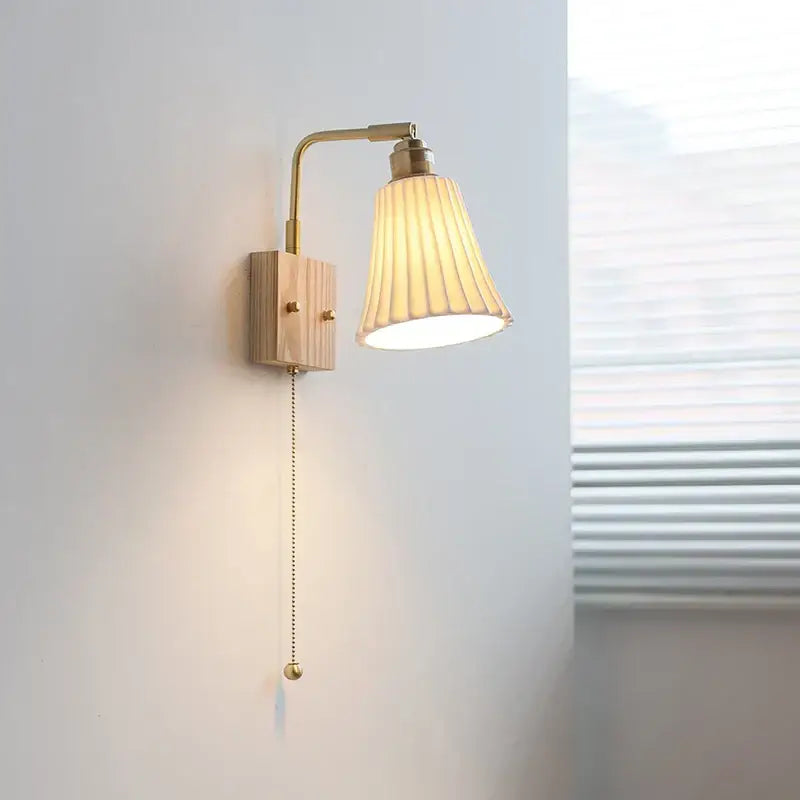 Modern brass and wood ceramic led wall sconce with pleated off-white glass shade and pull-chain switch for bedroom vanity light