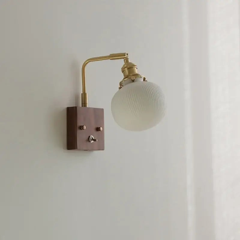 Modern brass and wood wall light fixture with off-white ribbed glass globe and toggle switch on dark wood base