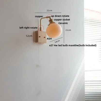 Copper-finished wall light fixture with matte ceramic globe shade and modern brass and wood elements for bedroom use