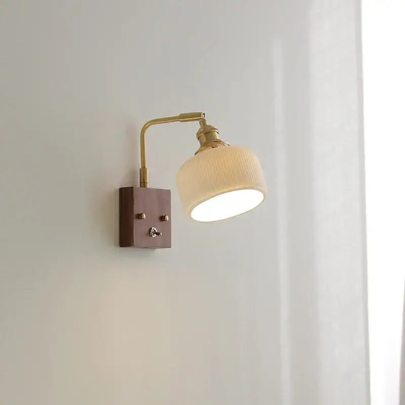 Modern brass and wood wall light fixture with warm-toned brass, ribbed off-white fabric shade, and dark wood base