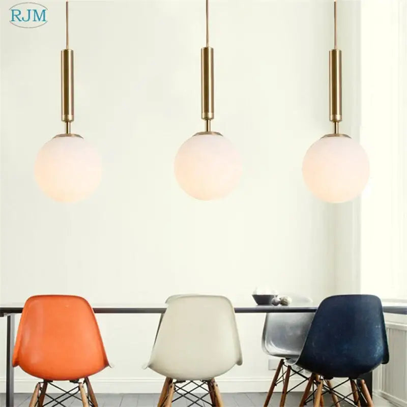 Three modern brass pendant lights with black decorbites glass ball led shades hang above a dining table