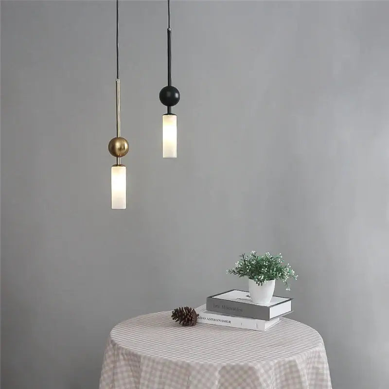 Two minimalist pendant lights with brass and black glass spheres hang above a checkered tablecloth for dining