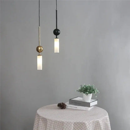 Two minimalist pendant lights with brass and black glass spheres hang above a checkered tablecloth for dining