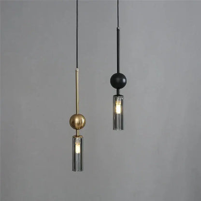 Two modern pendant lights with brass and black spheres and cylindrical glass shades for dining room design style