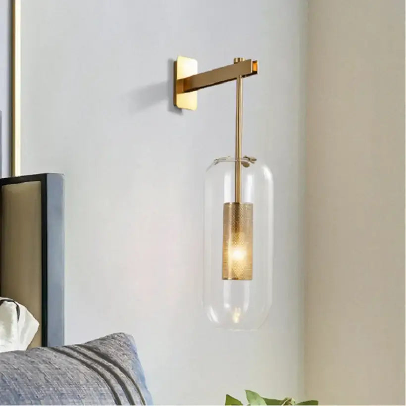 Modern brass and black wall sconce lights with clear glass housing and textured gold-finished cylindrical bulb for bedroom use