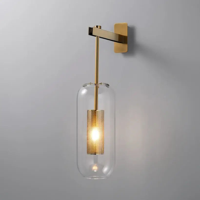Modern brass and black wall sconce light with gold-toned metal mesh shade and clear glass cylinder for bedroom use