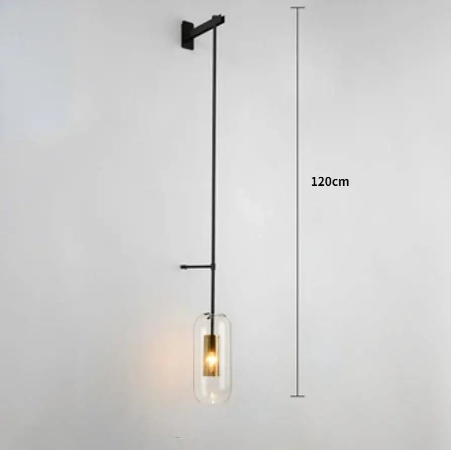 Modern brass and black wall sconce lights with a cylindrical glass shade and exposed brass filament bulb for bedrooms