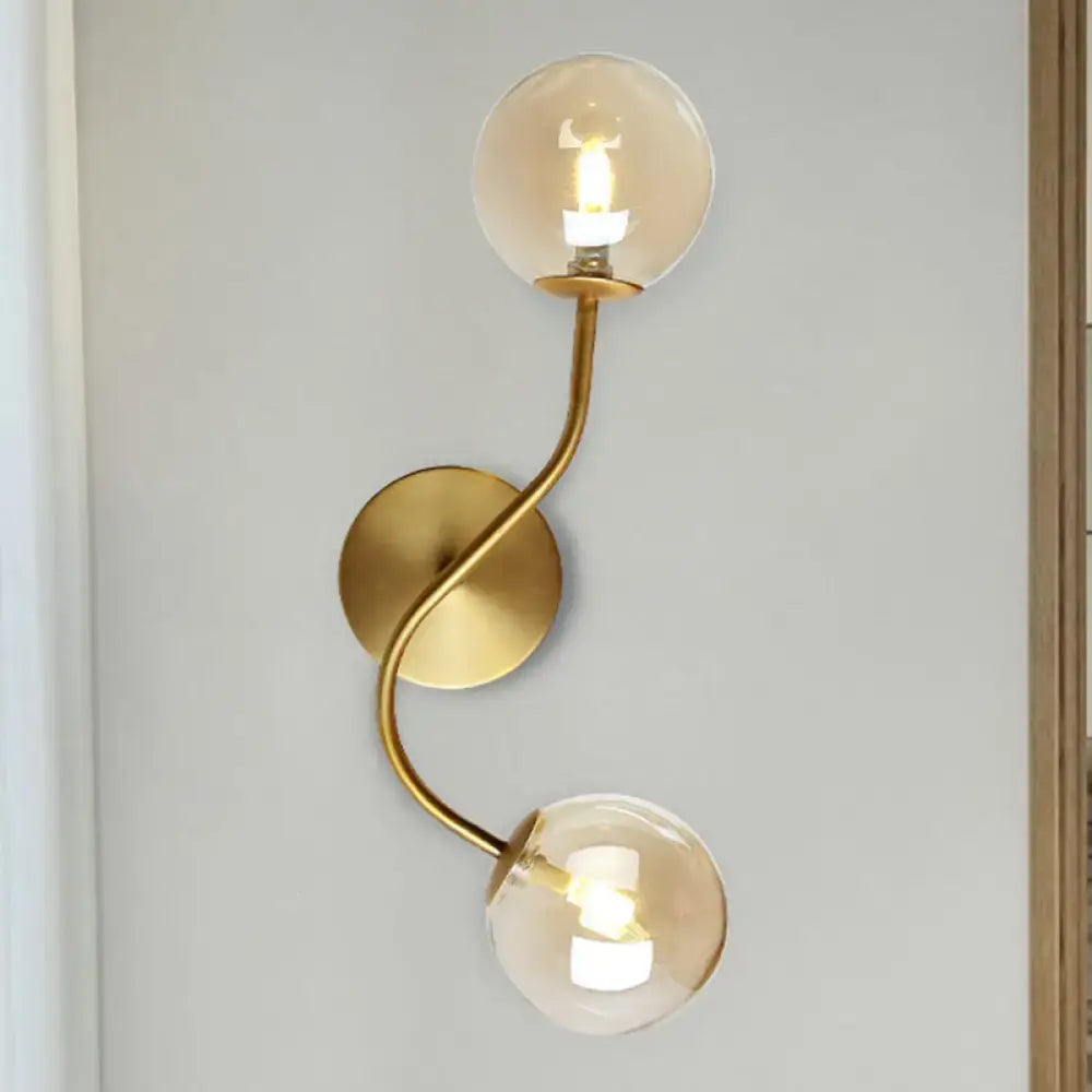 Modern brass clear tan glass wall lamp with gold-toned curved twisted arm and two spherical bulb base globes