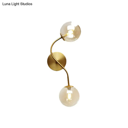 Modern brass clear tan glass wall lamp with gold-toned wall sconce and two curved arms each ending in bulb base