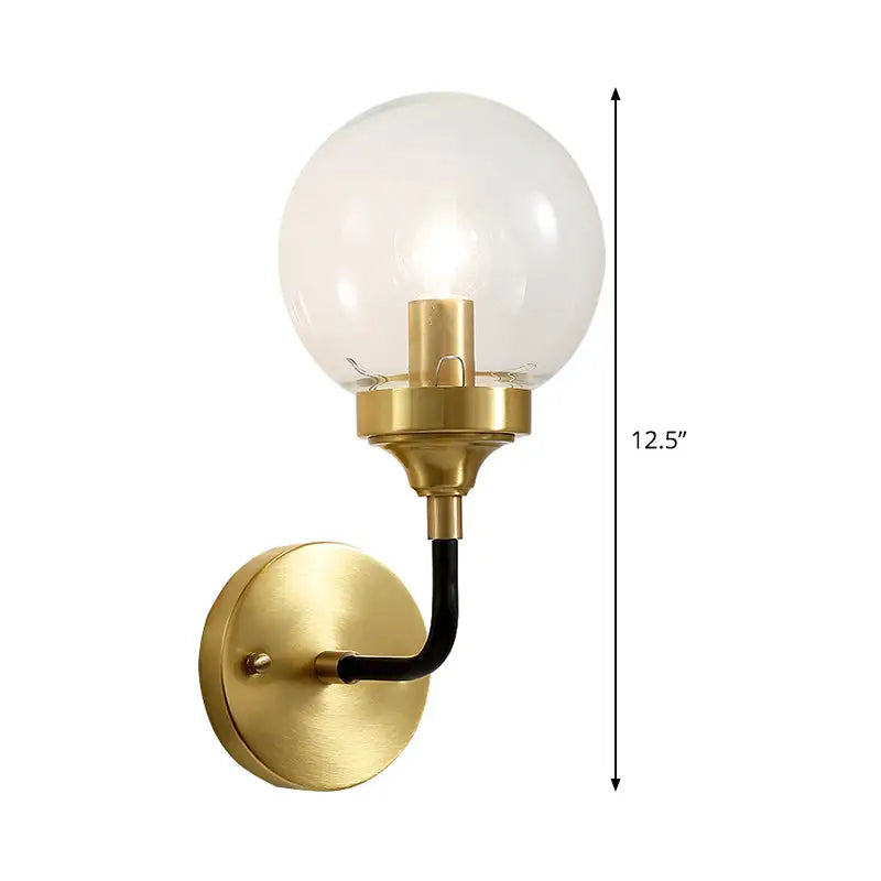 A modern brass wall sconce with a curved black arm and clear glass spherical bulb for bedroom lighting