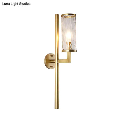 Modern brass cylinder sconce with gold finish and textured clear water glass shade for bedroom wall lighting