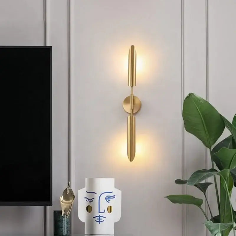 Modern brass cylindrical wall light with two vertical arms and circular base emitting warm light for decorbites golden luxury wall