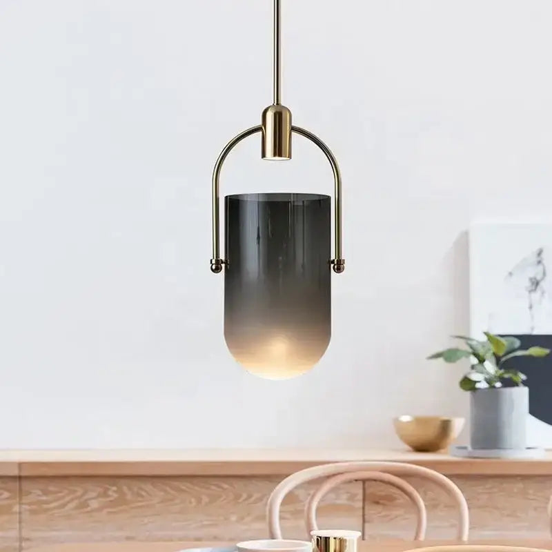 A modern brass decorbites bucket chandelier with a brass frame and cylindrical glass shade featuring amber tones