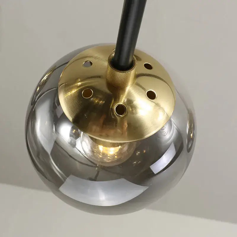 A sleek spherical decorbites glass ball led pendant light with polished brass mounting and black stem for kitchen lighting