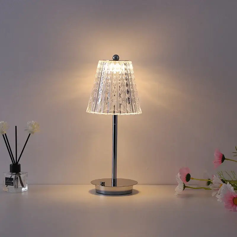 A modern brass diamond touch desk lamp with a clear faceted glass shade and polished chrome base for bedroom use