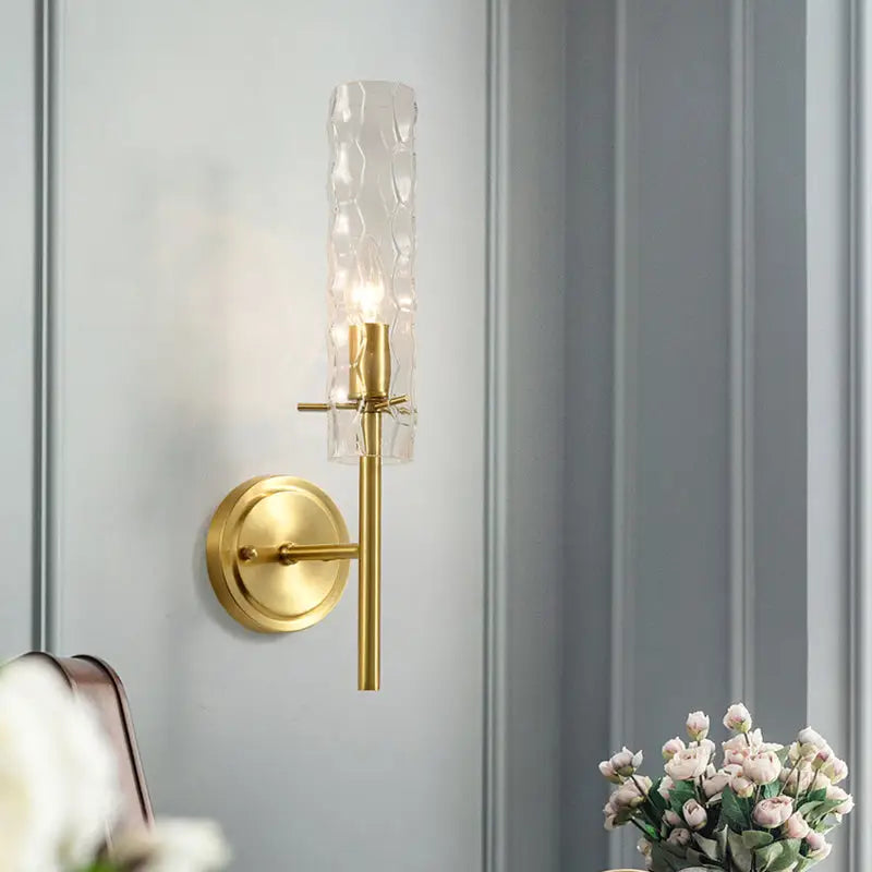 Modern brass wall light with gold-toned finish and dimpled blown glass cylinder shade for bedroom sconce lighting