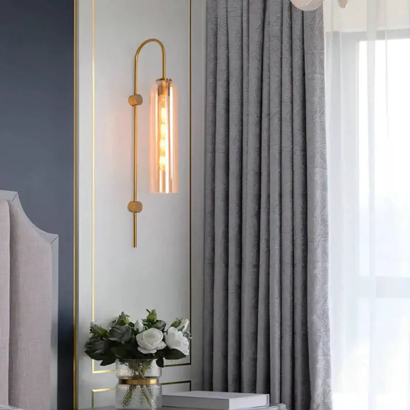 Modern brass e27 glass wall light with gold-toned curved arm and cylindrical glass shade for bedroom wall light