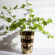 A modern decorbites geometric vase in stacked brass with a reflective finish holding vibrant green foliage decorbites geometric vase