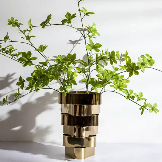 A modern decorbites geometric vase in stacked brass with a reflective finish holding vibrant green foliage decorbites geometric vase