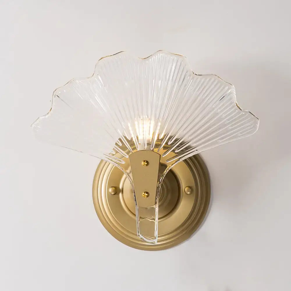 Modern brass ginkgo leaves wall light featuring a clear glass fan-shaped sconce with metallic accents for bedroom use