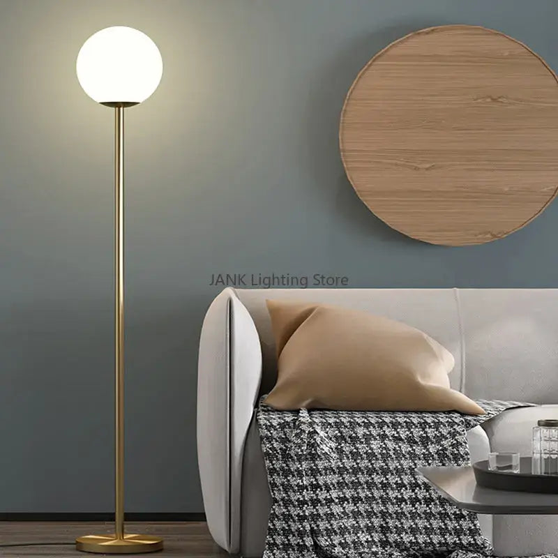 A sleek modern floor lamp with a brass finish and frosted glass ball by Decorbites for bedroom and study decor