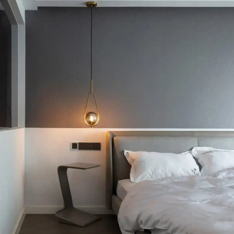 A sleek gold-toned decorbites glass ball pendant lighting with teardrop frame hangs above the bedroom bed