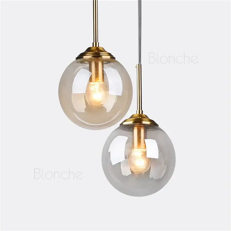 Two modern brass decorbites glass ball pendant lights with warm glowing bulbs for dining room decor