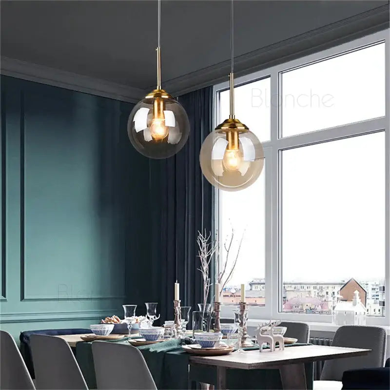Two elegant brass-finished decorbites glass ball pendant lights with translucent smoked glass globes hang above dining table