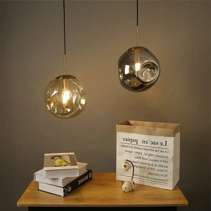 Two modern brass glass ball pendant lights with amber and frosted silver glass hang above a wooden table