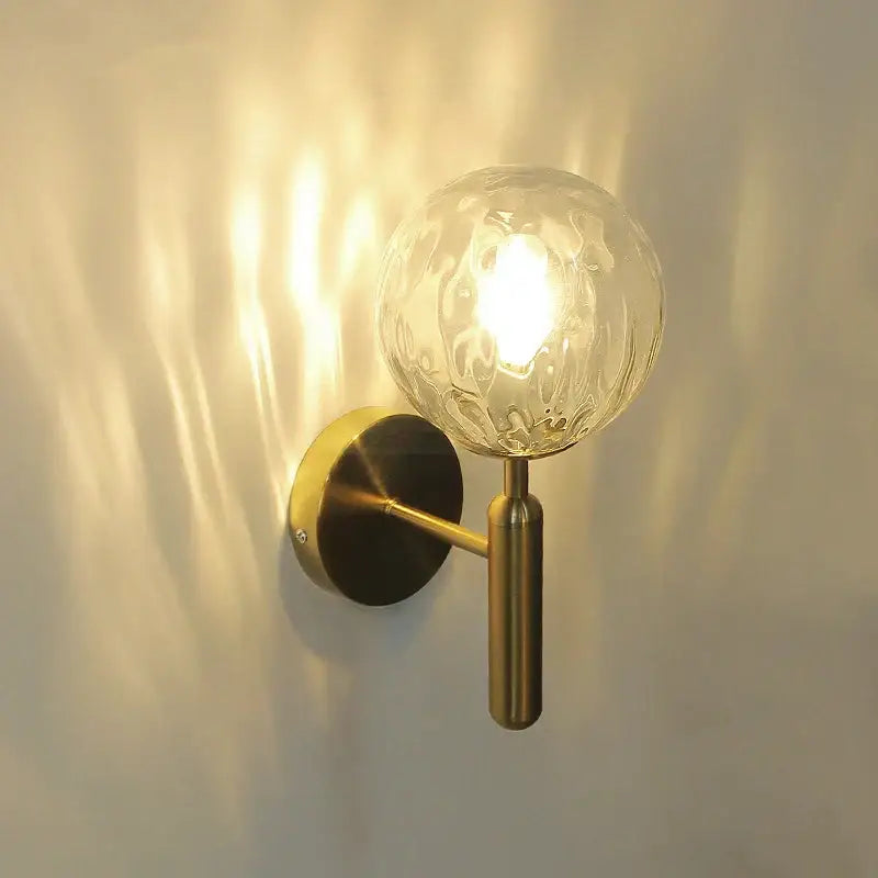 Modern brass glass ball wall lamp with a brass finish and textured clear glass globe for elegant bedroom decorbites wall lamp